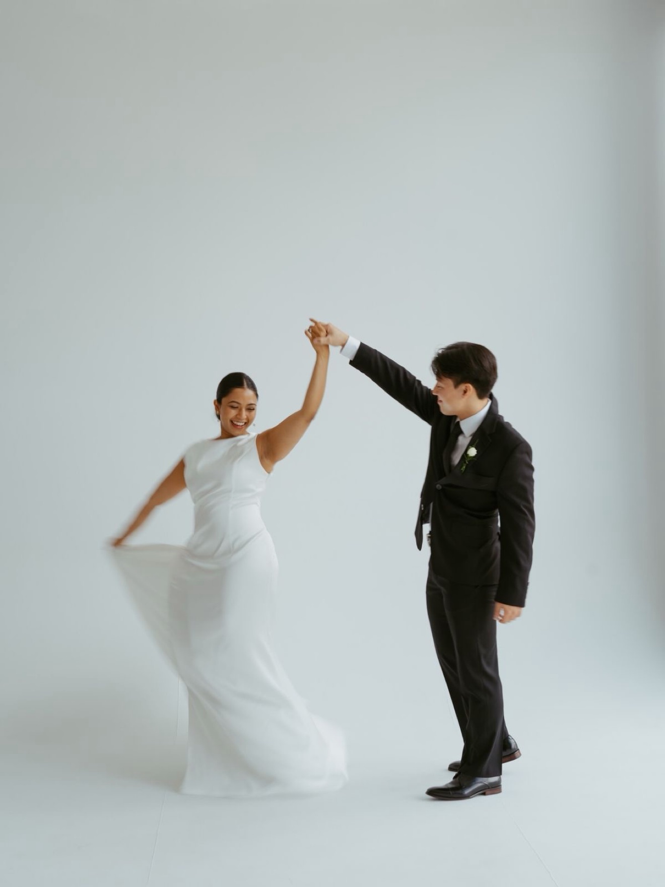 Bride in a white dress twirling as her groom spins her in a white studio, photographed by Kamar photography