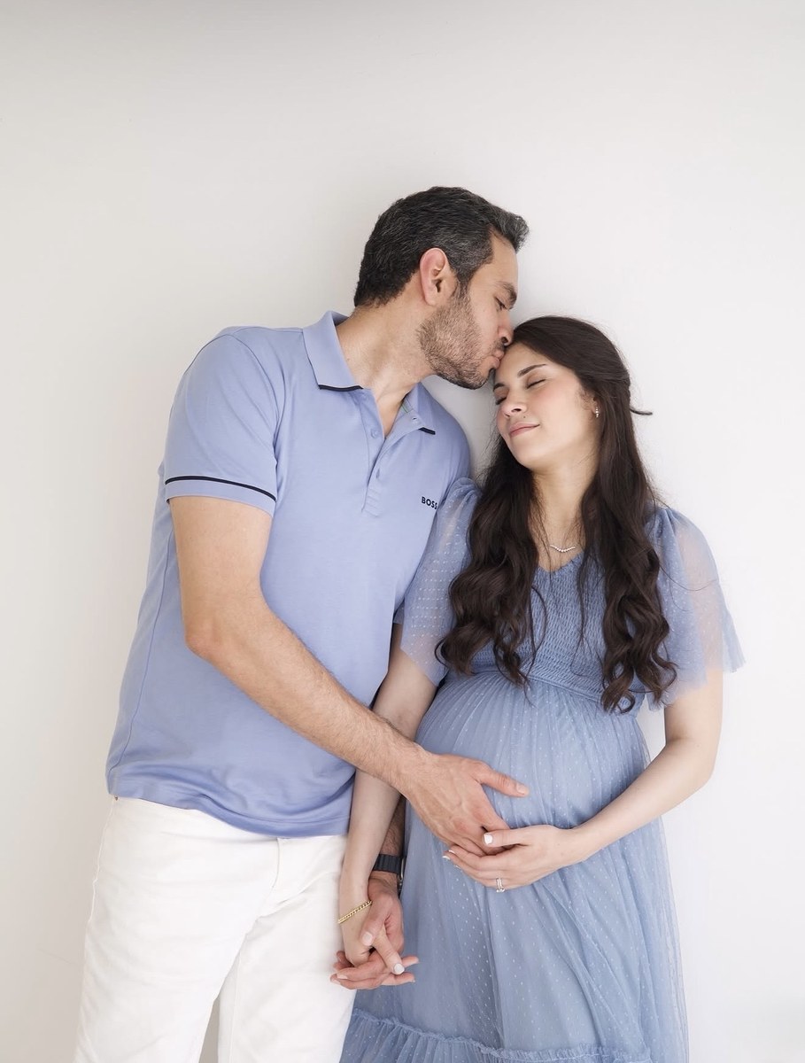 Pregnant woman in a blue dress standing with her partner, photographed by Kamar photography