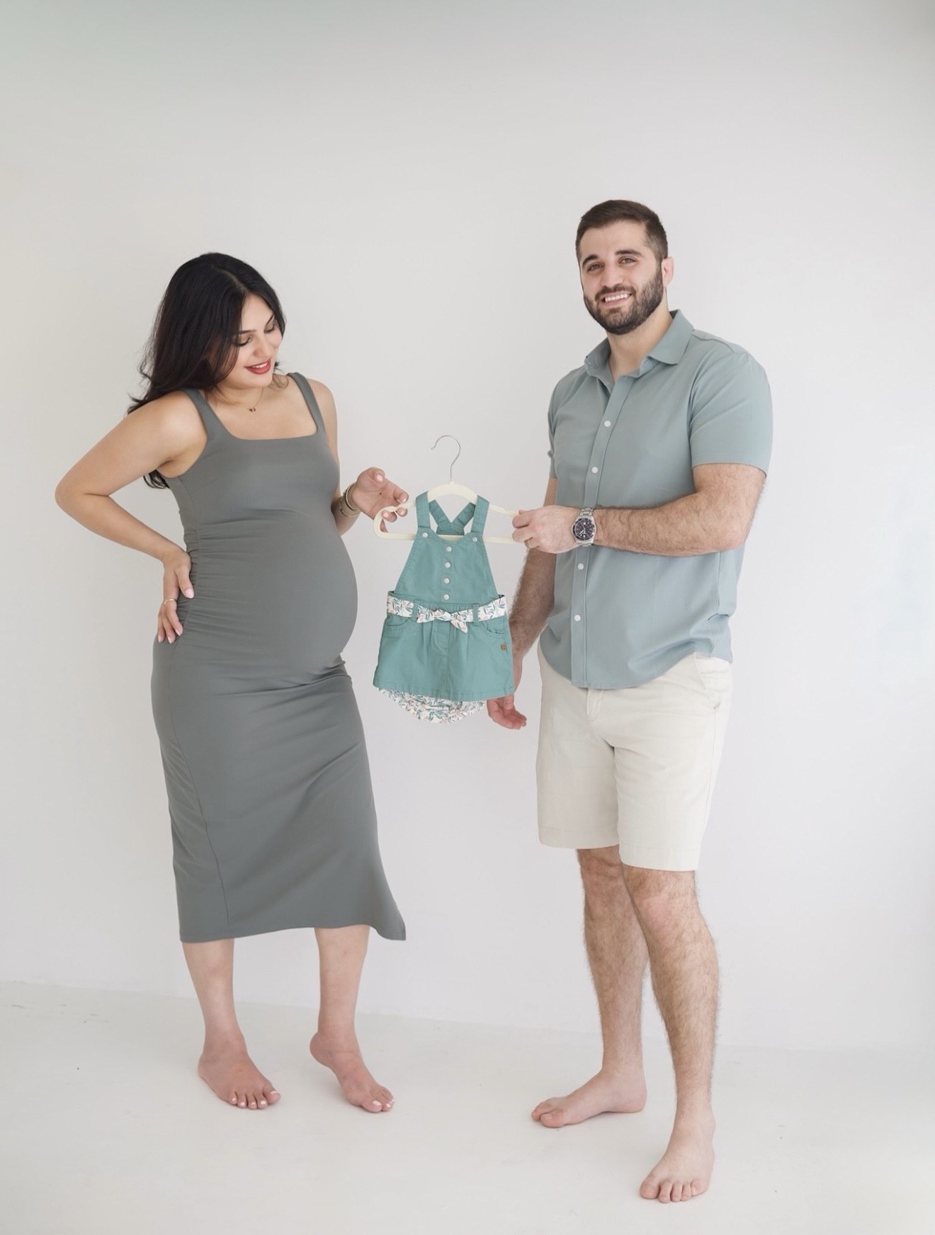 Pregnant woman in a gray dress holding an ultrasound with her partner, photographed by Kamar photography