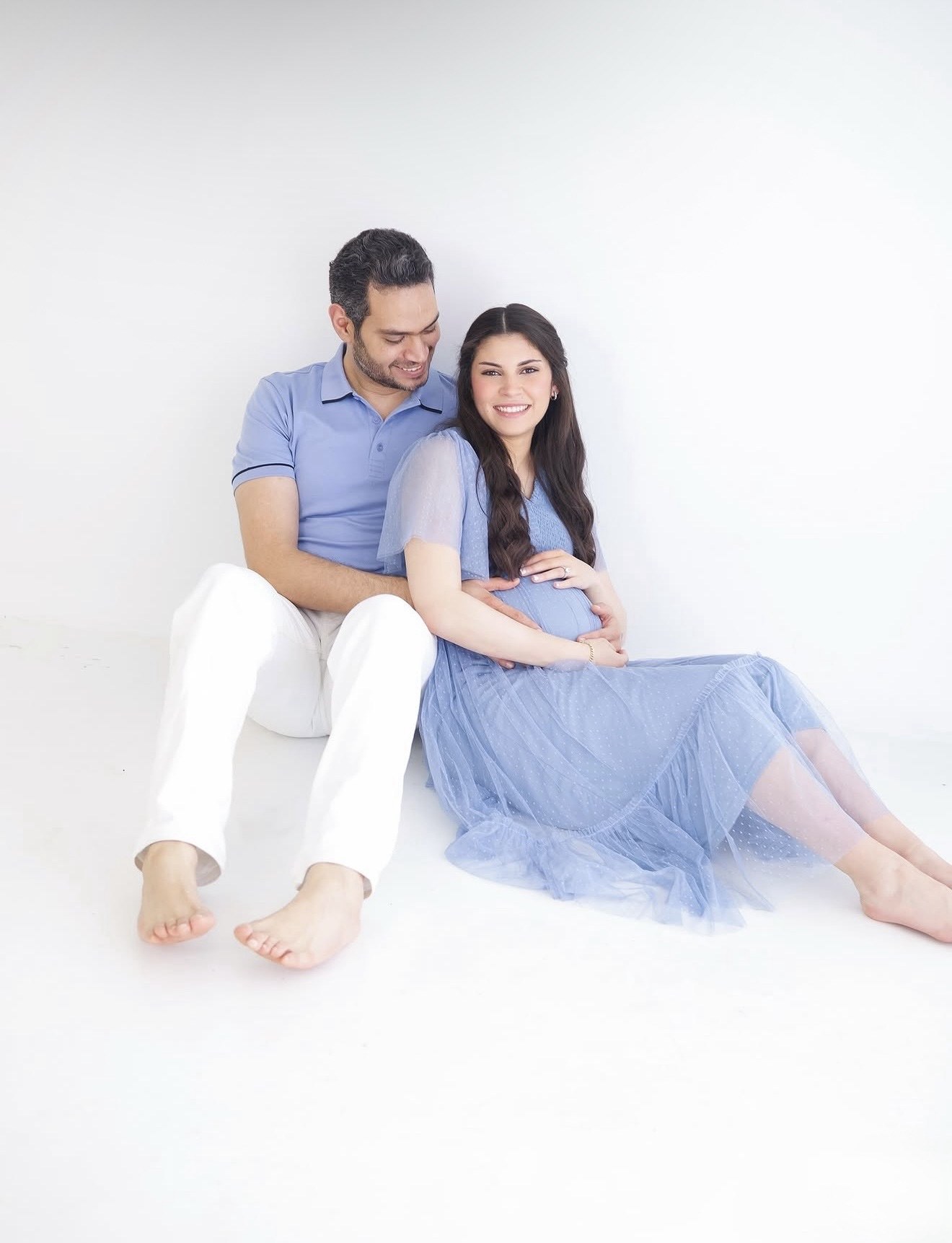 Pregnant woman in a blue tulle dress seated with her partner, photographed by Kamar photography