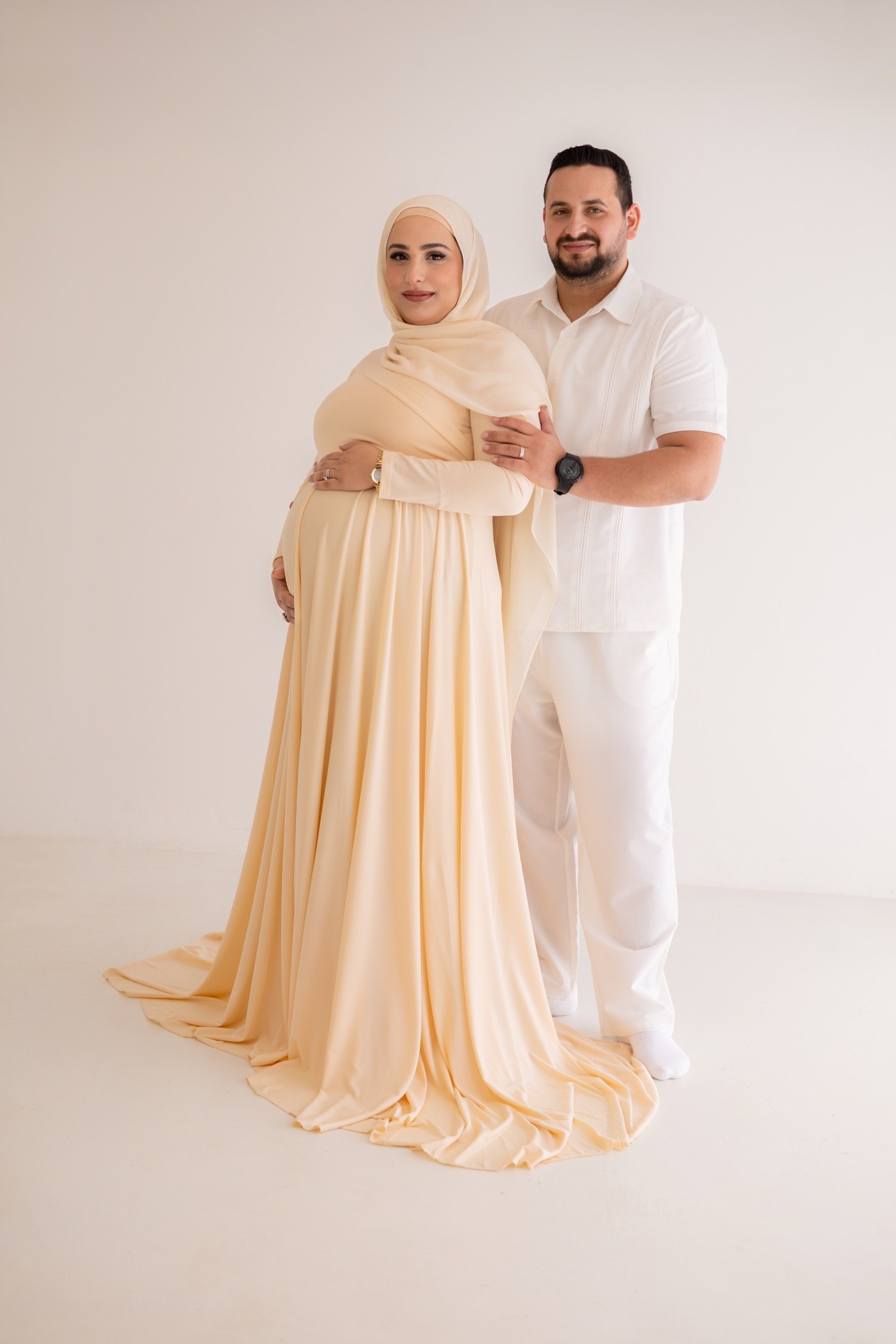 Pregnant woman in a peach gown standing with her partner, photographed by Kamar photography