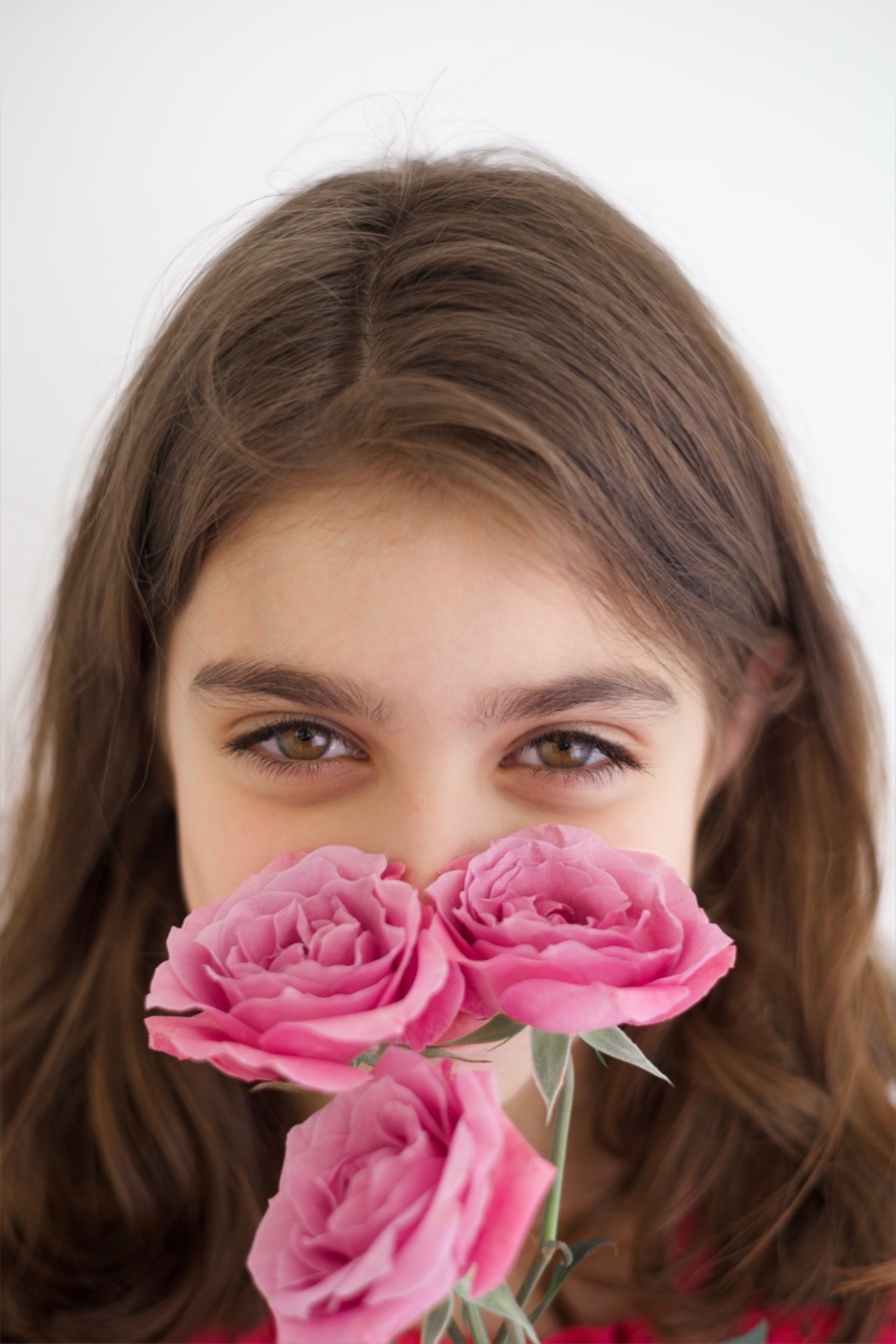 Young girl peeking over bright pink roses, photographed by Kamar photography